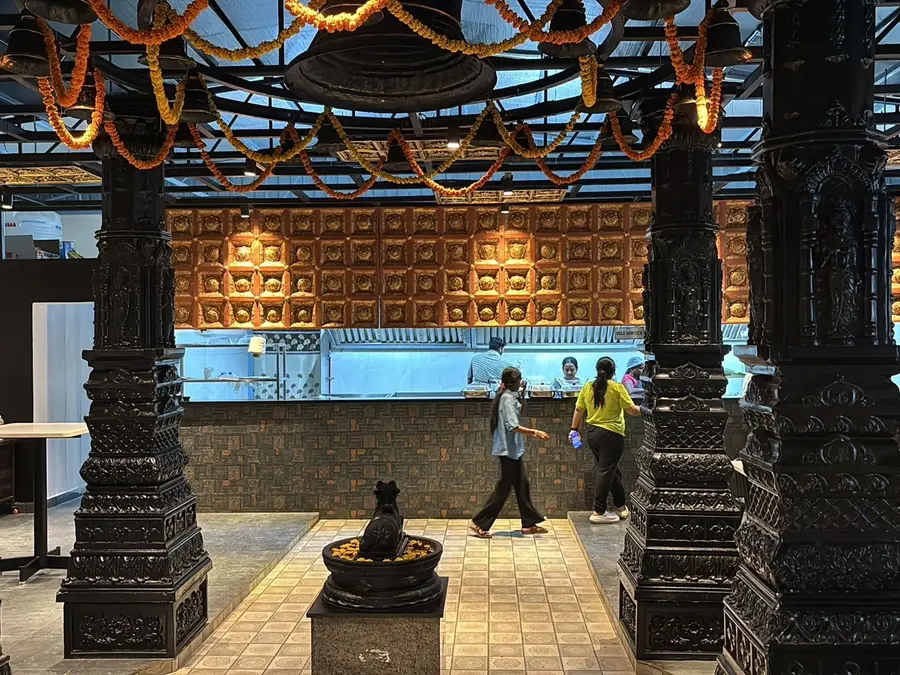 The entrance: carved granite pillars, an embossed brass wall behind the counter, marigold garlands overhead.