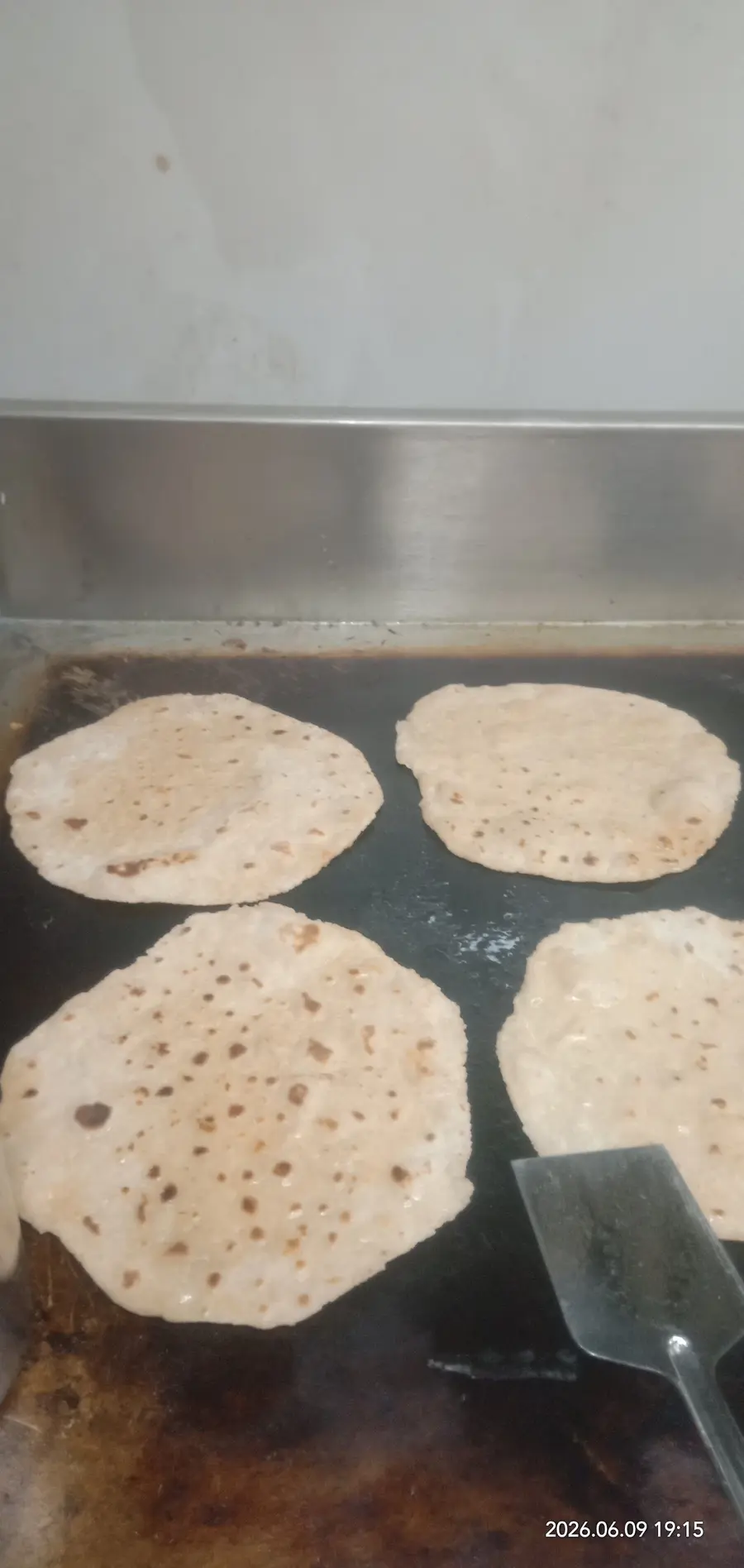 Four pooris puffing on a wide steel griddle.