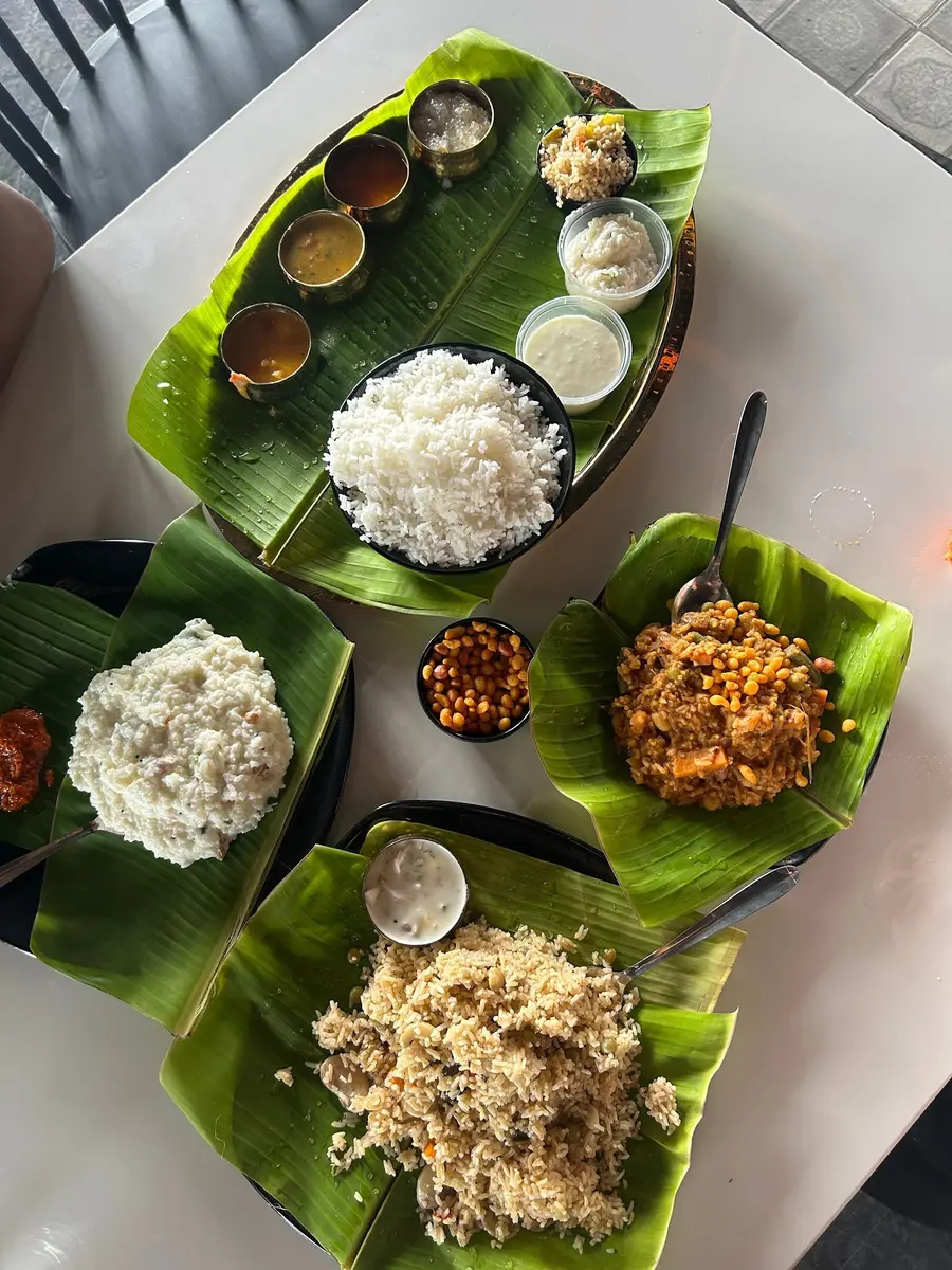A midday meal laid out on banana leaf: white rice, a second rice, dark curry, boondi, chutney and small steel cups of sambar.